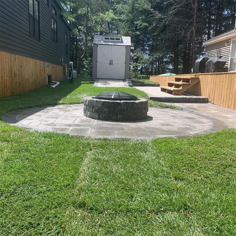 Circular interlock patio around a stone fire pit in a backyard